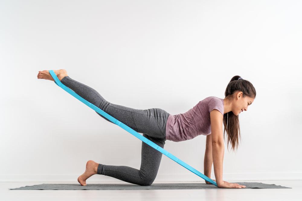 Resistance band fitness girl doing leg workout donkey kick floor exercises with rubber strap elastic. Glute muscle activation with kickback for cellulite.