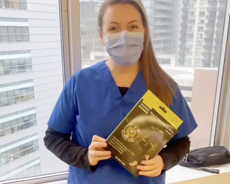 Nurse holding Mass & Slim Leggings Black package in front of a window with city view, nurse testimonial for TheBlackPurple.com.