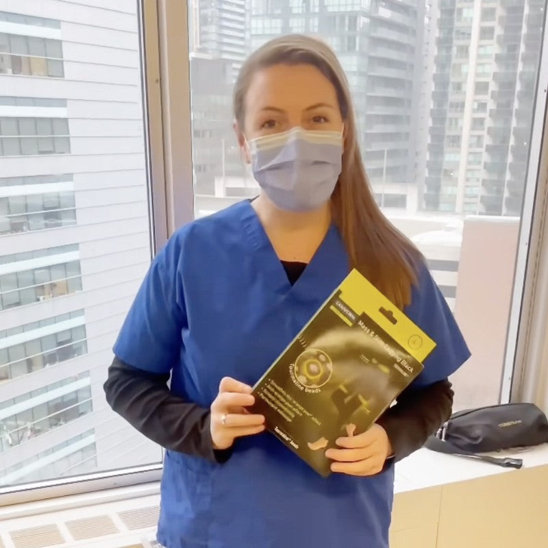 Nurse holding Mass & Slim Leggings Black package in front of a window with city view, nurse testimonial for TheBlackPurple.com.