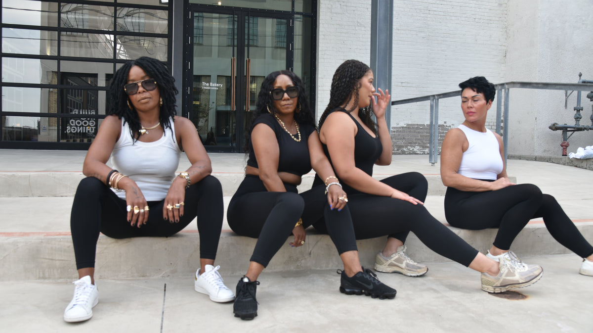 Four women wearing black leggings and athletic tops sitting outdoors